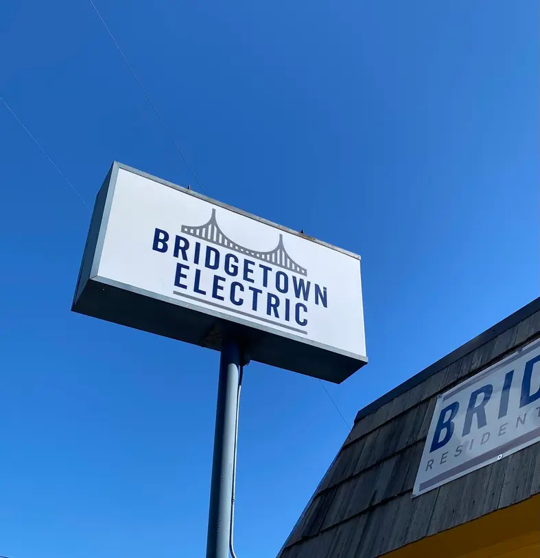 The Bridgetown Electric pole sign, a navy hexagon with a suspension bridge mark, against a clear Portland sky