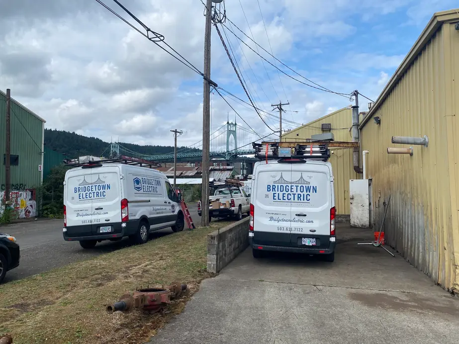 Two wrapped Bridgetown Electric vans parked at a Portland job site with the St. Johns Bridge behind them