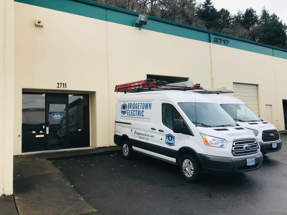 A wrapped Bridgetown Electric van with a loaded ladder rack parked outside the shop