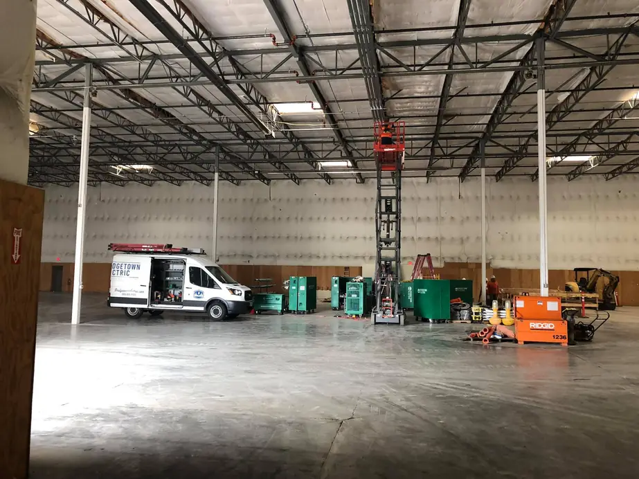Commercial warehouse mid electrical rough-in with distribution panels on carts and a Bridgetown Electric van inside